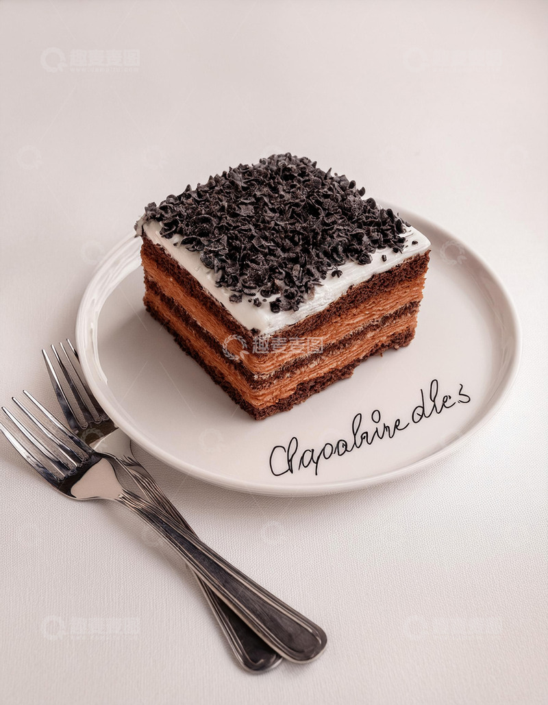 一块放在白色盘子上夹着奶油顶部撒有巧克力屑的方形蛋糕旁边有把银勺和银叉