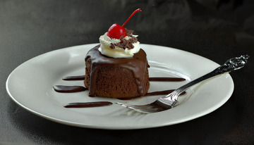 放在白色盘子上淋着巧克力酱顶部有颗樱桃和奶油的巧克力蛋糕