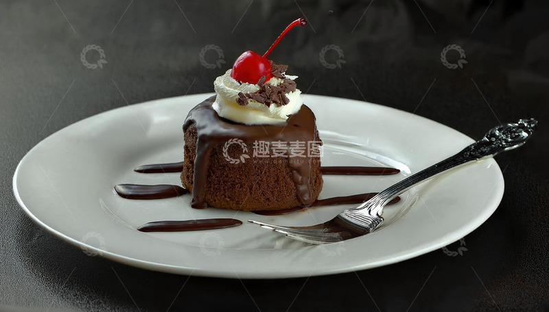 放在白色盘子上淋着巧克力酱顶部有颗樱桃和奶油的巧克力蛋糕