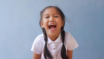 一位扎着双马尾，穿着白色上衣，张大嘴巴露出灿烂笑容的小女孩