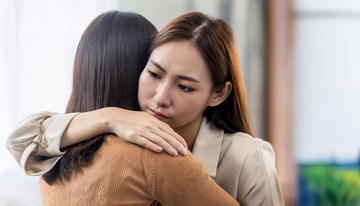 两位女性相拥其中一位面露哀伤的场景