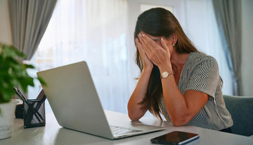 一位坐在桌前面对笔记本电脑用手掩面表现出哀伤情绪的女性1