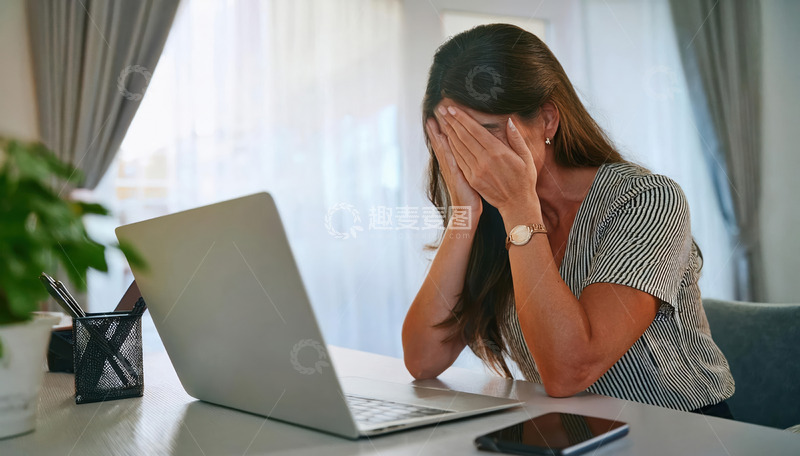 高清大图下载【趣麦麦图】-一位坐在桌前面对笔记本电脑用手掩面表现出哀伤情绪的女性1