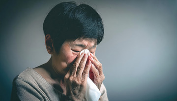 一位头发灰白的老年女性手持纸巾擦拭，流露哀伤神情