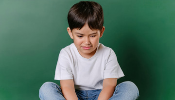 小男孩坐在绿色背景前展现出哀伤神情