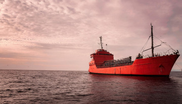 红货船在粉紫天际下的海洋航行