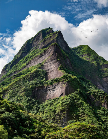 蓝天下绿覆峭壁的巍峨高耸山峰