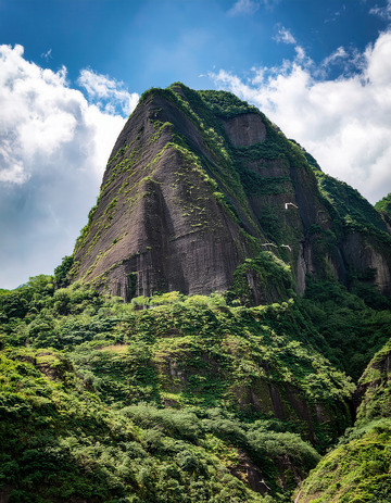 蓝天下植被披覆的巍峨陡峭山峰