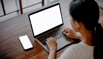 女士在木桌前使用电脑与手机