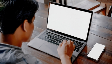 男子于木桌前操作电脑与手机