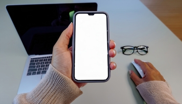 手在桌前持空白屏手机与电脑等