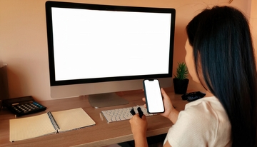 女士桌边操作手机与空白屏电脑