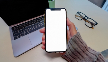 手持白屏手机，旁置电脑与眼镜