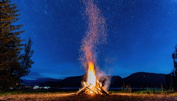 星空下湖畔燃烧迸溅火花的篝火