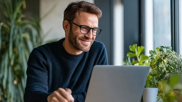 戴眼镜的男子在室内使用笔记本电脑微笑