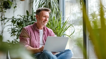 男子窗边使用笔记本电脑微笑着望向窗外