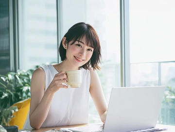 办公室内微笑女子手持咖啡杯与笔记本电脑