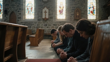 教堂内众人低头祈祷光线透过彩色玻璃窗