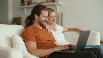 情侣在沙发上使用笔记本电脑微笑互动