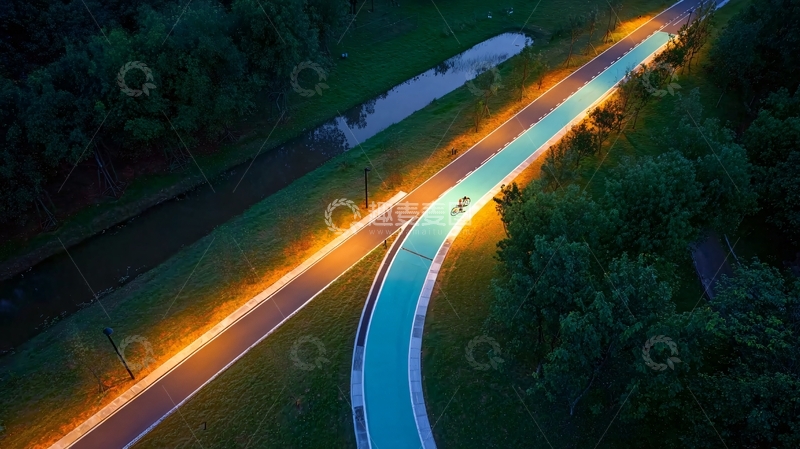 高清大图下载【趣麦麦图】夜晚灯光下的弯曲自行车道与绿树环绕的宁静场景