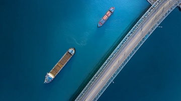 俯瞰视角下桥梁旁的两艘货船航行于碧蓝水域